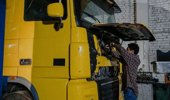 Skilled mechanic inspecting a yellow truck engine in a repair shop.