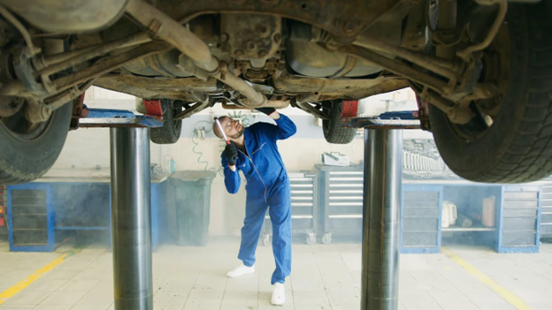 Mechanic inspecting vehicle underside during auto body repair service.