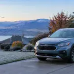 Sleek gray SUV parked outside with mountain and lake background.