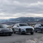 Three luxury cars parked on mountain road with scenic background.