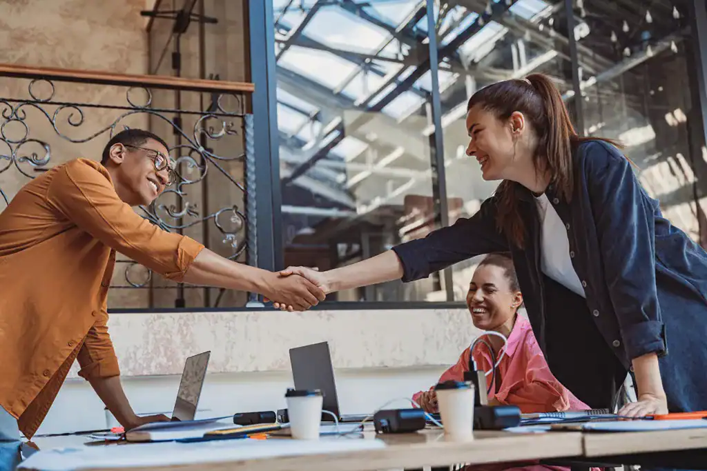 Smiling business professionals shaking hands in modern office space.