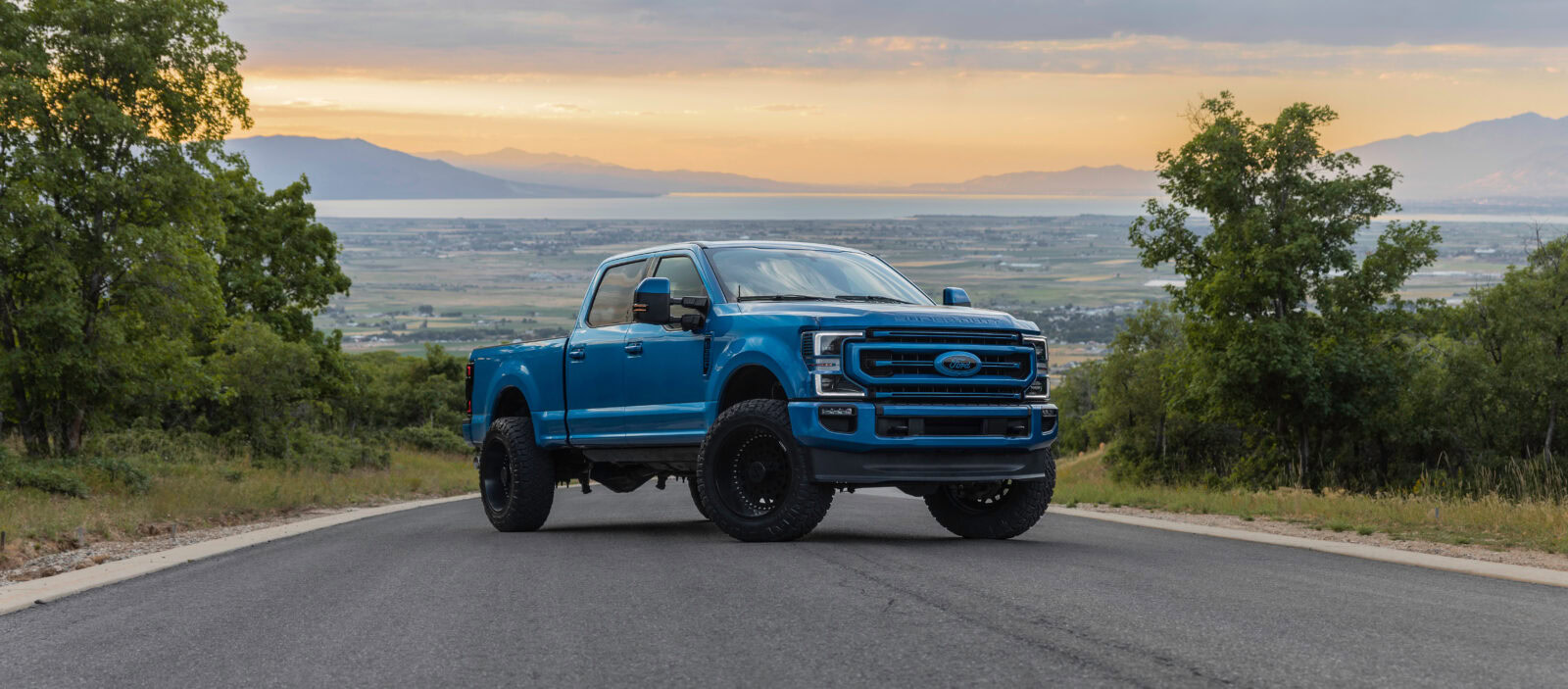 Ford truck on open road with scenic mountain and sunset background.