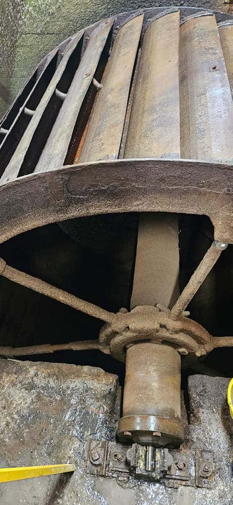 the historic all-iron overshot waterwheel, showing its buckets, shrouds, main shaft and bolt-on stub axle