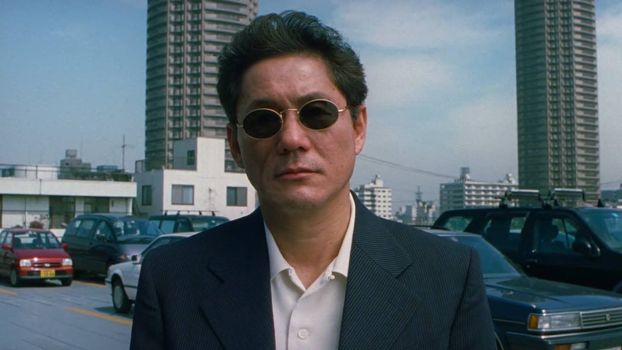 Takeshi Kitano in HANA-BI wearing sungloasses in a parking lot