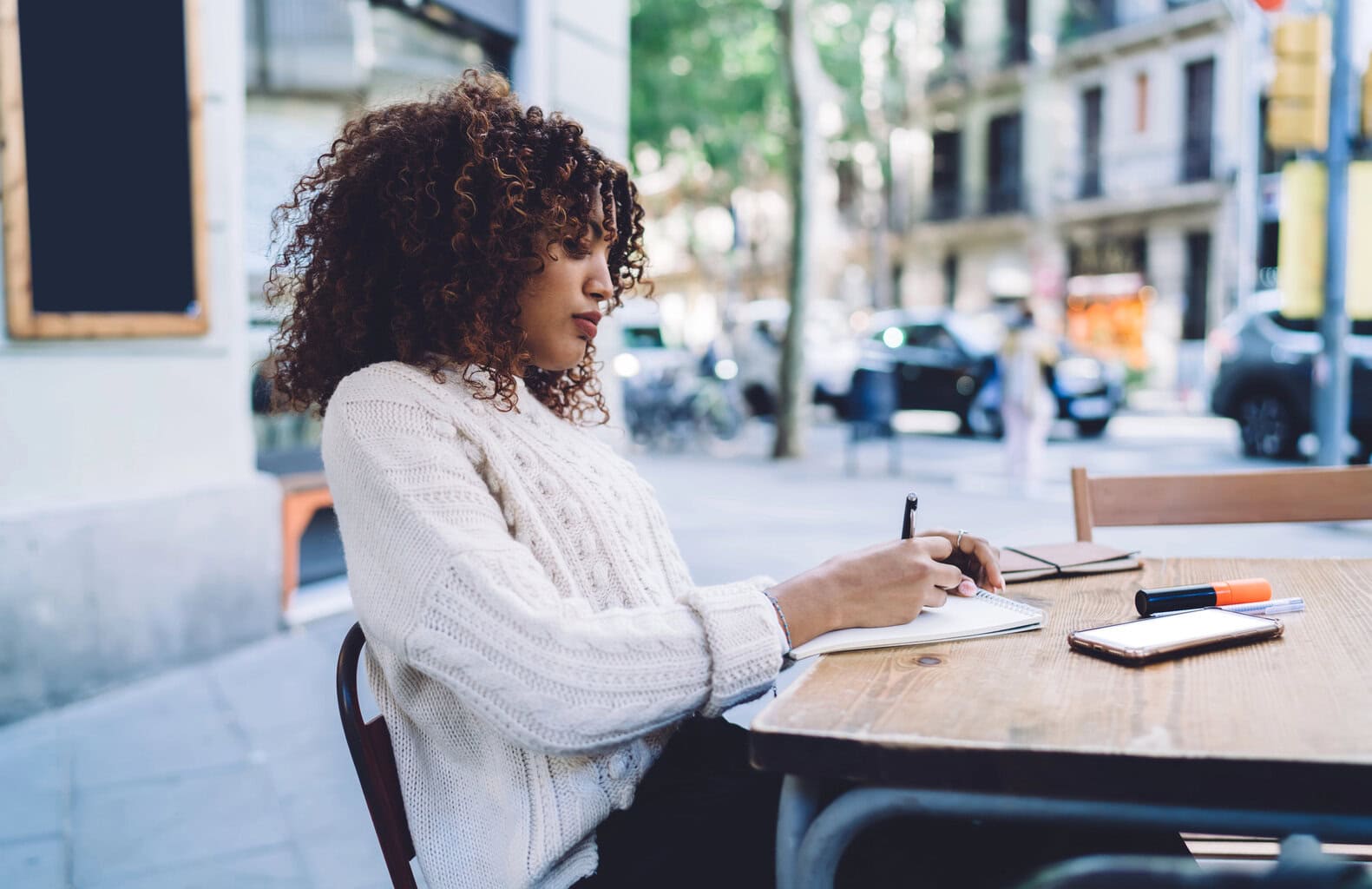 Woman focused on journaling at an outdoor cafe, representing clarity and hormone balance