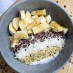 Fresh banana slices, shredded coconut, chia seeds, and quinoa in a healthy smoothie bowl topped with creamy yogurt. A nutritious breakfast featuring natural ingredients for a delicious start to your day.
