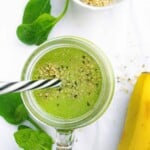 Fresh green smoothie with chia seeds in a glass jar, surrounded by spinach leaves and banana, on a white background for a healthy eating lifestyle.