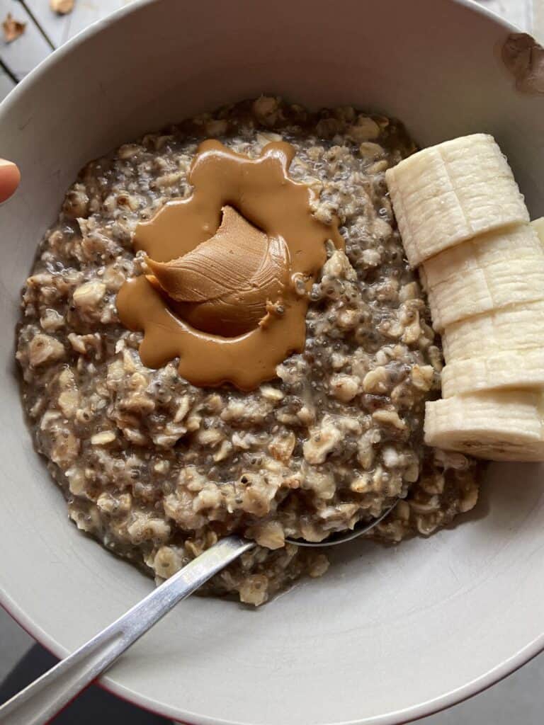 Creamy peanut butter oatmeal topped with a spoonful of peanut butter and sliced bananas in a white bowl. Healthy breakfast featuring oats, bananas, and natural peanut butter for energy and nutrition.