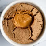 Soft-baked peanut butter skillet cookie with melted peanut butter center in a white ramekin on marble surface.
