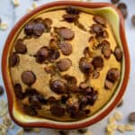 Creamy chocolate chip cookie skillet in a rustic ceramic dish with scattered oats and chocolate chips around it, perfect for a delicious homemade dessert.