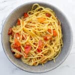Savory spaghetti pasta with cherry tomatoes and herbs served in a gray bowl on marble surface.