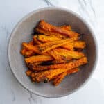 Crispy roasted sweet potato fries in a gray ceramic bowl on a white marble surface, perfect for healthy snacking or meal prep.