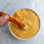 Creamy cheese and bacon dip served in a white bowl on marble surface, featuring melted cheese and crispy bacon strips for a delicious snack or appetizer.