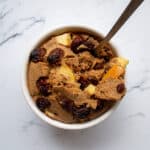 Creamy apple cinnamon baked oatmeal topped with dried cranberries in a white bowl. Perfect healthy breakfast packed with fiber and flavor, enjoy nourishing start to your day.