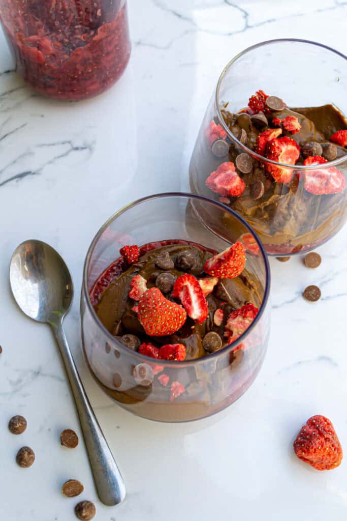 Fresh strawberry chocolate mousse dessert in glass bowls topped with chopped strawberries and chocolate chips, served on a marble countertop with a spoon.