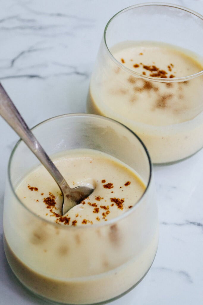Creamy vanilla panna cotta dessert topped with cocoa powder in clear glass bowls on a marble surface. Elegant and delicious, perfect for summer gatherings or special occasions. Great for dessert recipes and food presentation.