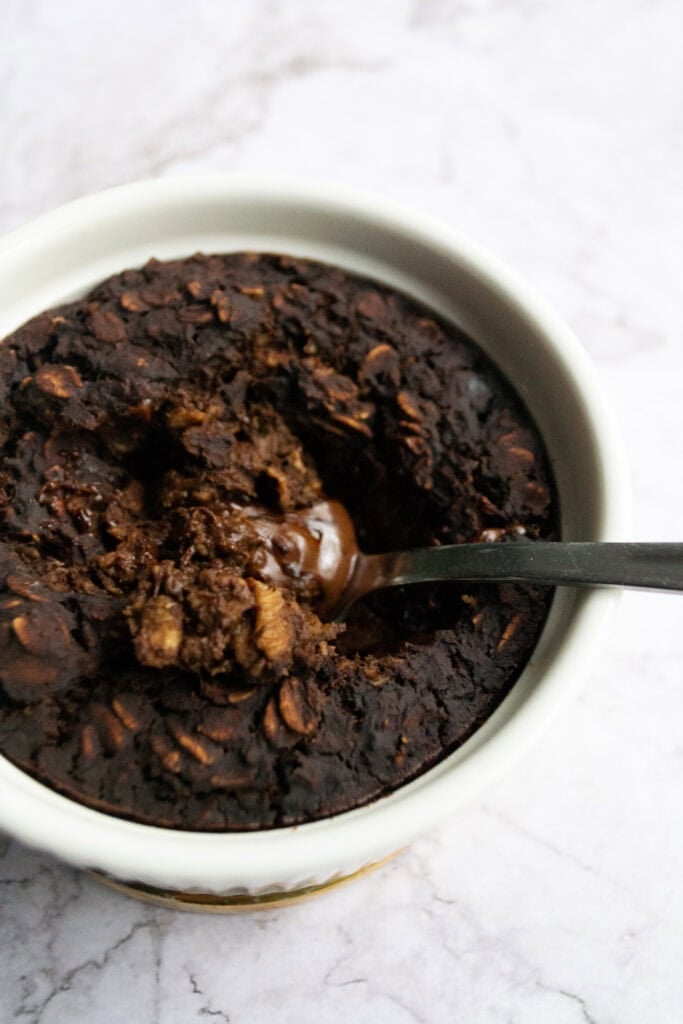Top view of brownie batter baked oats with a spoon in it and melted chocolate in the centre.