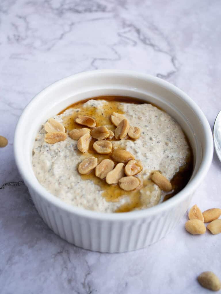 Creamy tahini dip topped with roasted peanuts and drizzled with honey, served in a white ceramic bowl on a marble surface. Perfect for healthy snacking or as a flavorful appetizer.