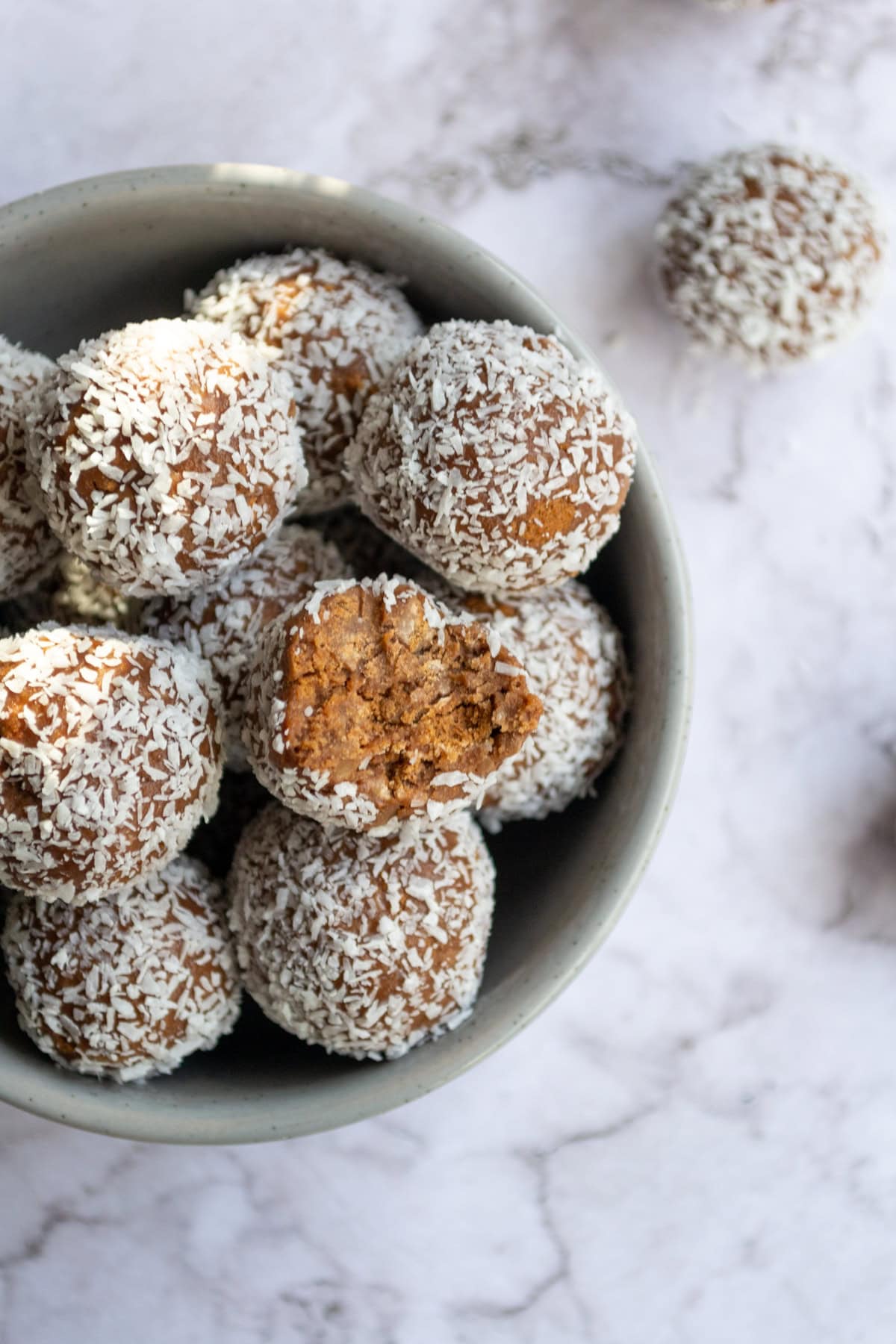 A bunch of Tim Tam balls in a grey bowl on a marble table.