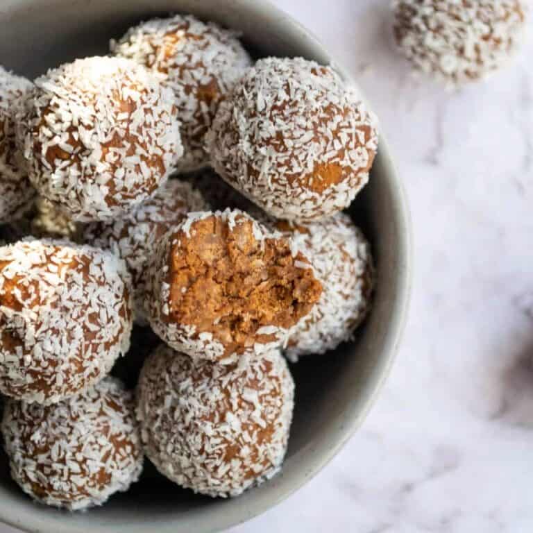 Sweet coconut macaroons with golden brown centers, coated in shredded coconut, served in a white bowl for delicious dessert treats.