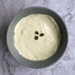 Creamy vanilla coffee pudding topped with three coffee beans, served in a gray bowl on a marble surface. Perfect for coffee-flavored desserts or a sweet treat.