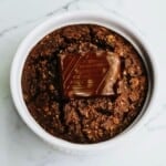 Rich chocolate brownie with a glossy chocolate piece on top, served in a white ramekin. Perfect for dessert lovers seeking indulgent, homemade-style sweet treats. Ideal for baking enthusiasts and chocolate fans.