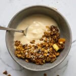 Butternut squash granola with yogurt and dried fruit in a metallic bowl on a white marble surface.