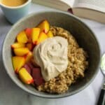 Creamy yogurt topping with fresh peach slices and oatmeal in a gray bowl, served with a cup of coffee and an open book in the background, emphasizing healthy breakfast ideas.