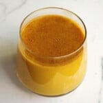 Creamy turmeric golden milk latte in a clear glass with a frothy surface, perfect for health and wellness. Rich in anti-inflammatory spices, ideal for cozy mornings or evening relaxation.