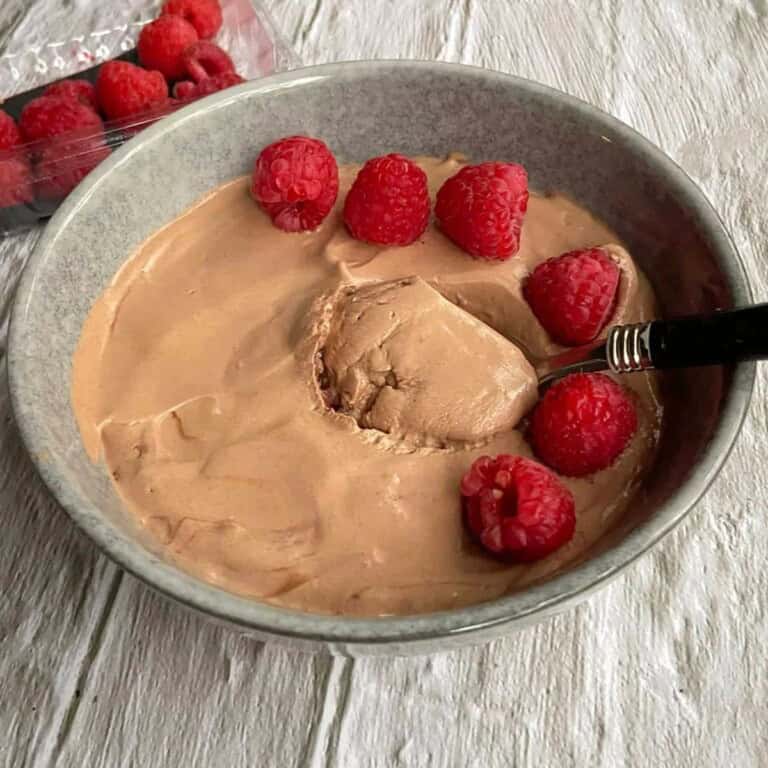 Creamy chocolate mousse topped with fresh raspberries on a gray ceramic bowl, ready to serve as a delicious dessert.