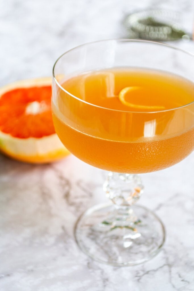 Grapefruit daiquiri in a crystal glass on a white marble table with a grapefruit in the background.