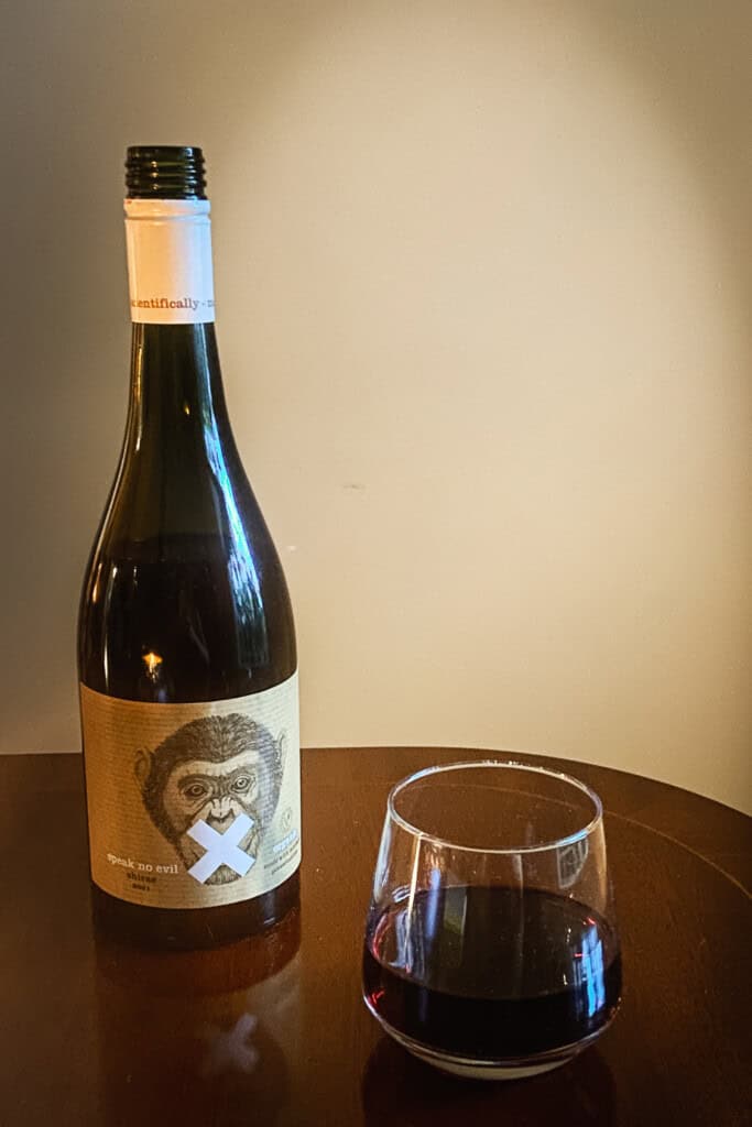 A bottle of Speak No Evil Shiraz next to a full wine glass.