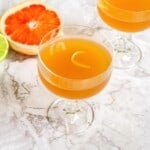 Refreshing citrus cocktail with grapefruit and lime garnishes, served in elegant glassware on a marble surface. Perfect for summer drinks and healthy, fresh fruit beverages.