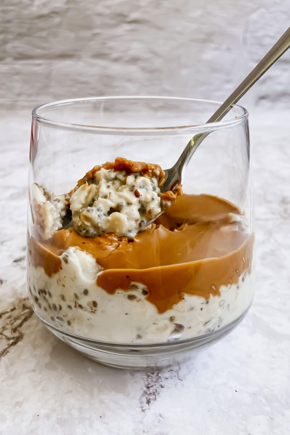 A spoon resting in a glass of overnight oats against a white background.