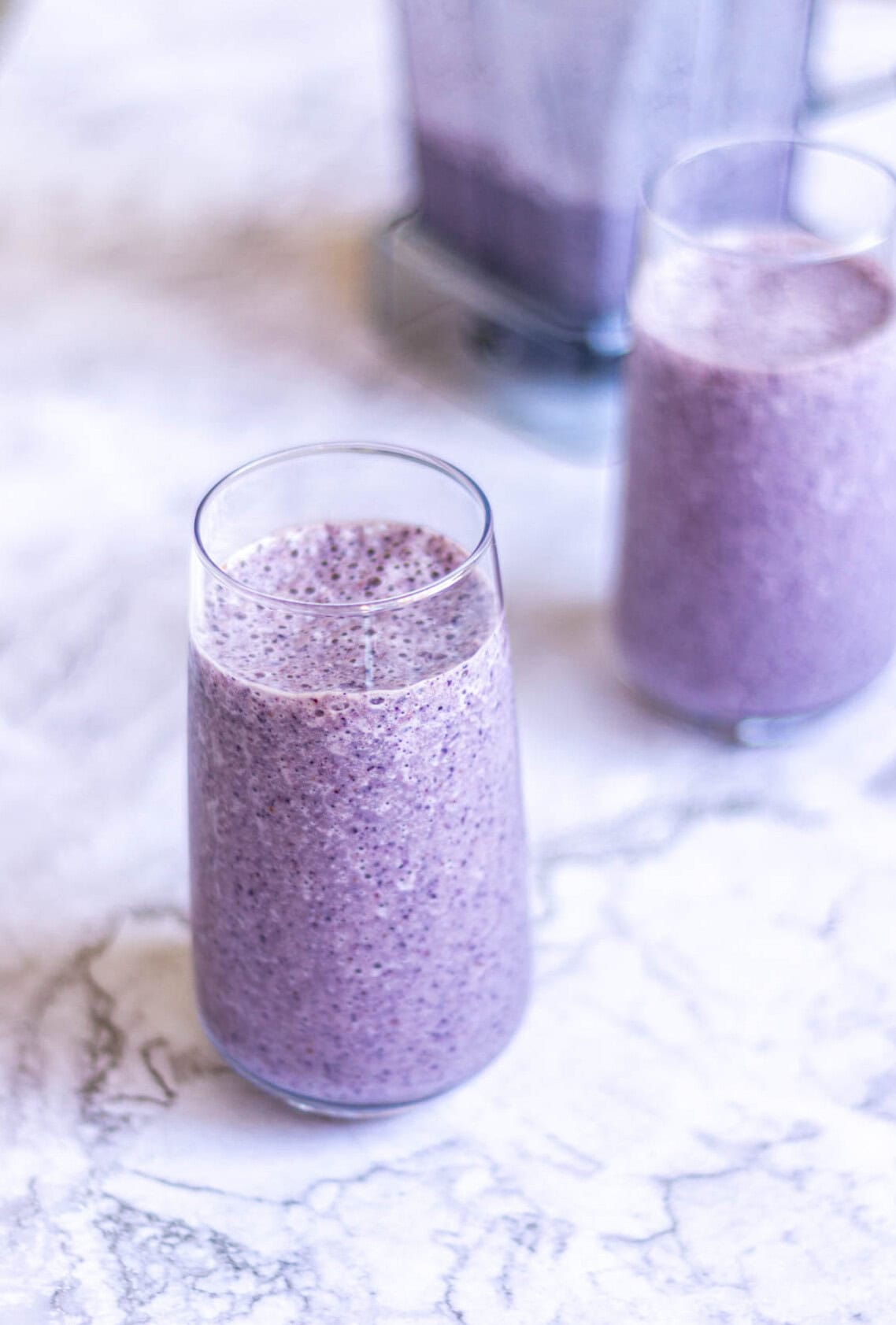 Creamy blueberry smoothie in tall glass with fresh berries, healthy breakfast, antioxidant-rich, vegan, dairy-free, nutritious drink.