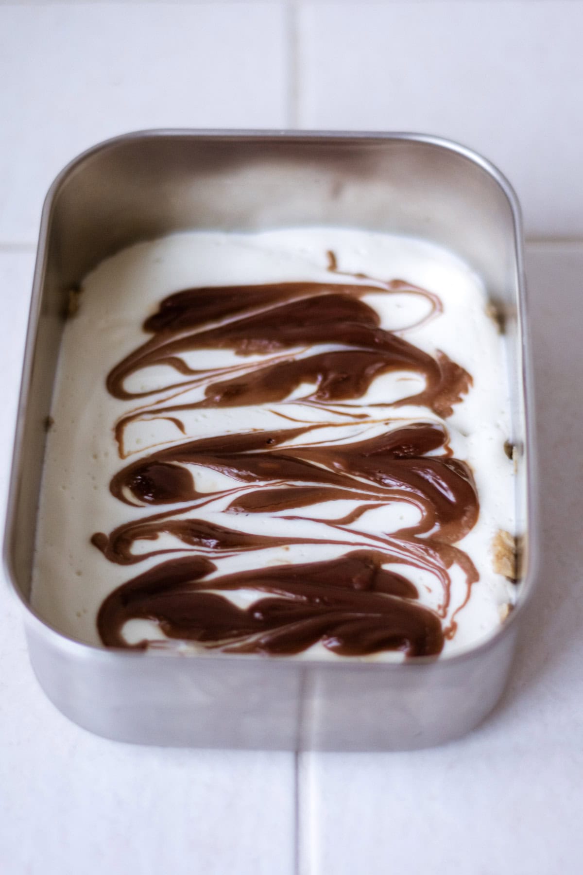 Creamy dessert with chocolate swirls layered on top in a metal container, perfect for sweet treats and dessert recipes.