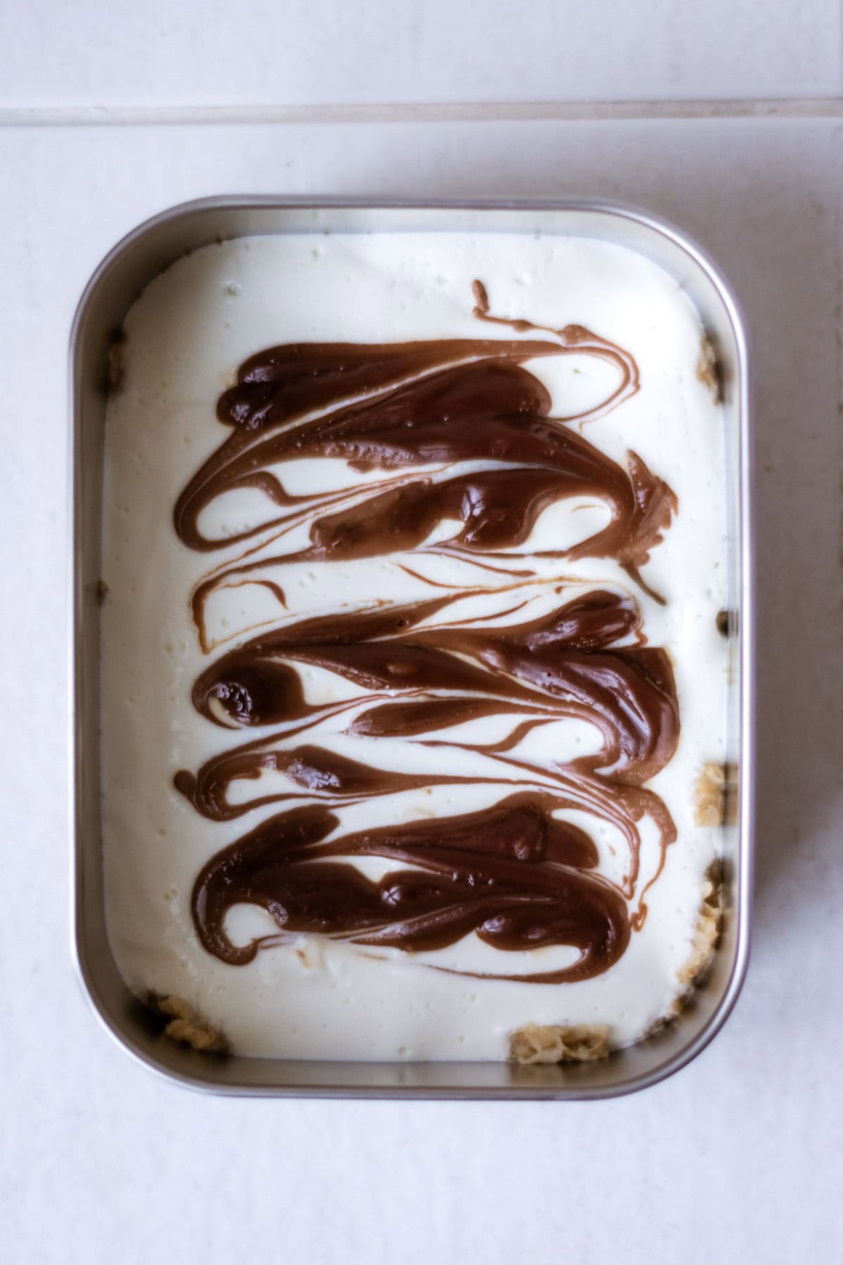 Creamy homemade ice cream with a rich chocolate swirl topping, served in a rectangular metal container, perfect for a delicious summer treat or homemade dessert.