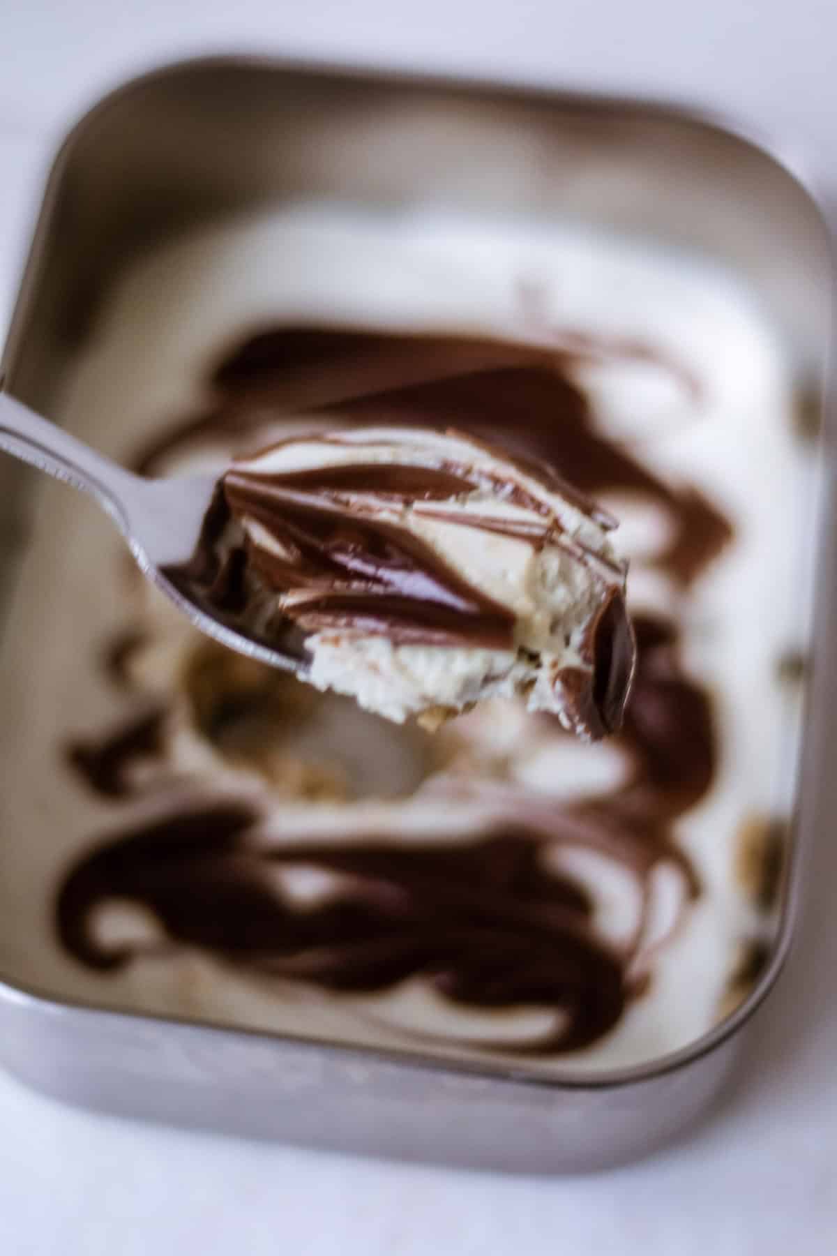 Rich and creamy vanilla ice cream with swirls of chocolate fudge, served in a metal container, perfect for a delicious dessert treat.