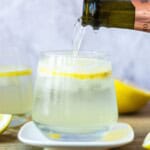 Refreshing lemon sparkling water served in a clear glass with ice, sliced lemons, and a lemon wedge in the background, perfect for healthy hydration and enhancing wellness.