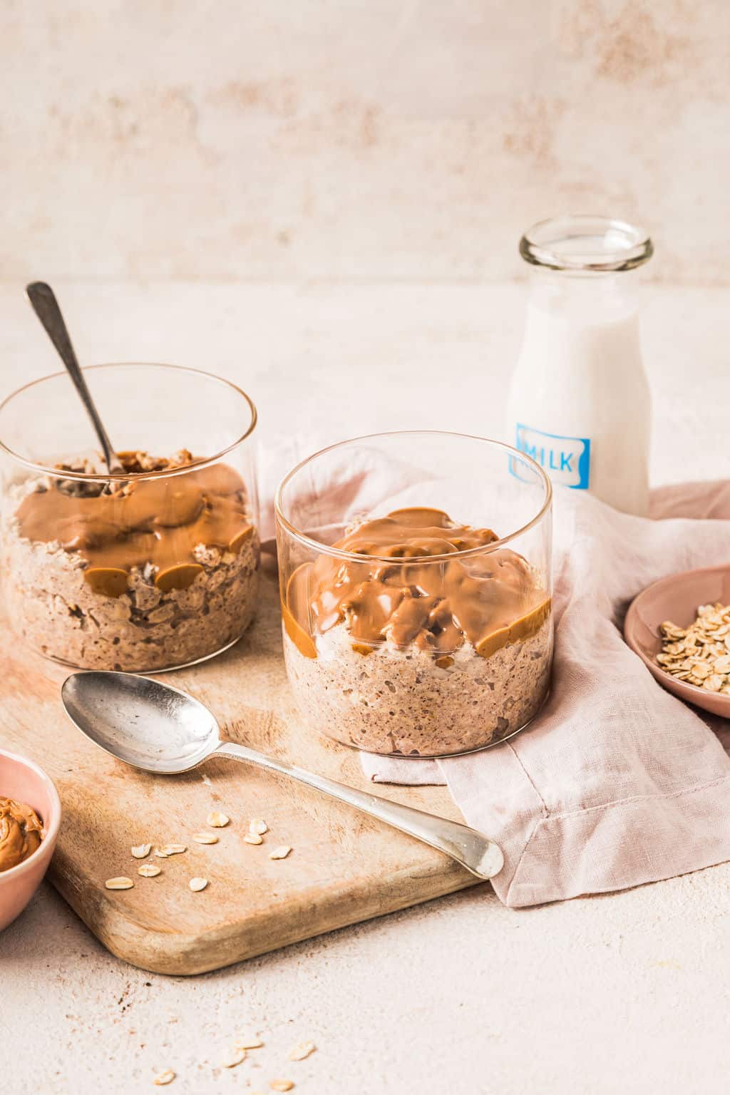 Creamy oatmeal topped with caramel sauce and served in glass bowls on a rustic wooden board with a jar of milk in the background, perfect for a healthy breakfast or snack.