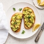 Creamy mashed avocado on toasted bread with herbs and spices, garnished with fresh parsley and lemon wedges. Perfect healthy breakfast or snack option with vibrant flavors and nutritious ingredients.