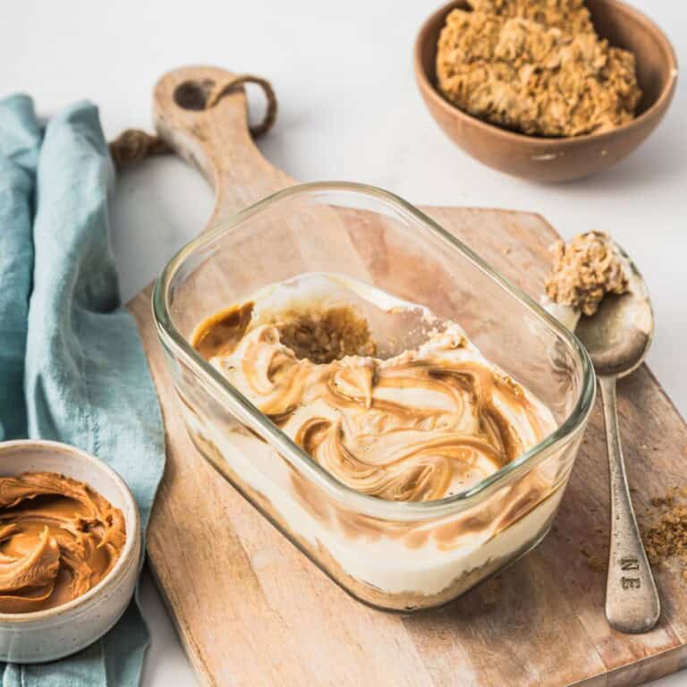 Creamy peanut butter and honey swirl ice cream in a glass baking dish with peanut butter, honey, and vanilla ingredients on a wooden cutting board.
