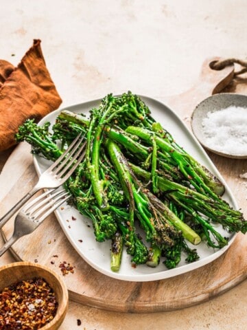Grilled asparagus on a white plate with seasoning, served with crushed red pepper flakes and sea salt, arranged on a rustic wooden cutting board for healthy vegetarian meal options.