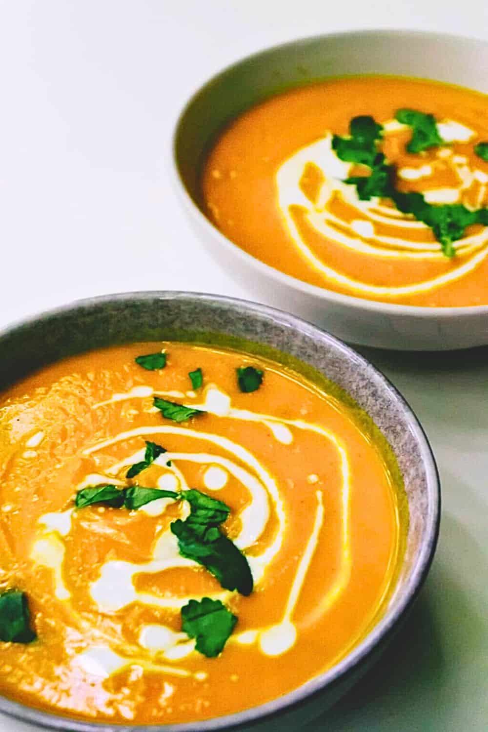 Creamy tomato soup with a swirl of cream and fresh cilantro garnishes, served in stylish bowls. Perfect for a comforting meal, this delicious soup is made with fresh ingredients for a wholesome, flavorful experience.