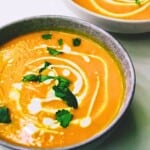 Creamy carrot ginger soup garnished with fresh cilantro and a swirl of cream, served in a rustic bowl. Perfect for healthy, homemade soups and comforting meals.