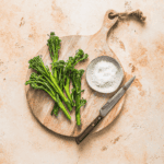 Fresh broccolini on a rustic wooden cutting board with salt and a knife, ideal for healthy cooking and nutritious recipes.