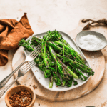 Roasted asparagus with salt and chili flakes on a white plate, served on a wooden round board, garnished with seasonings, with a rustic background for healthy, fresh veggie recipes.