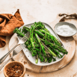 Sautéed pan-fried broccolini with seasoning, perfect for healthy meals and easy recipes, served on a white plate with salt and chili flakes for added flavor.