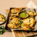 Savory baked Empanadas filled with vegetables and cheese, served with vibrant green chimichurri sauce for dipping. Perfect for appetizers or a flavorful snack from Simply Fresh Foodie.