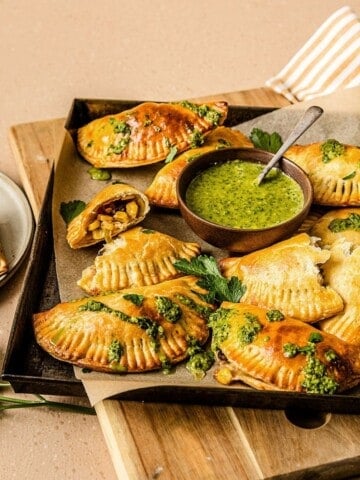 Savory baked Empanadas filled with vegetables and cheese, served with vibrant green chimichurri sauce for dipping. Perfect for appetizers or a flavorful snack from Simply Fresh Foodie.